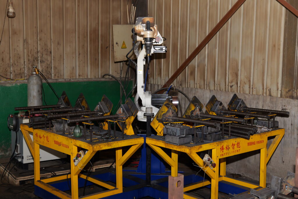 Automated welding robot arm manufacturing high precision steel prop threaded tubes inside factory workshop