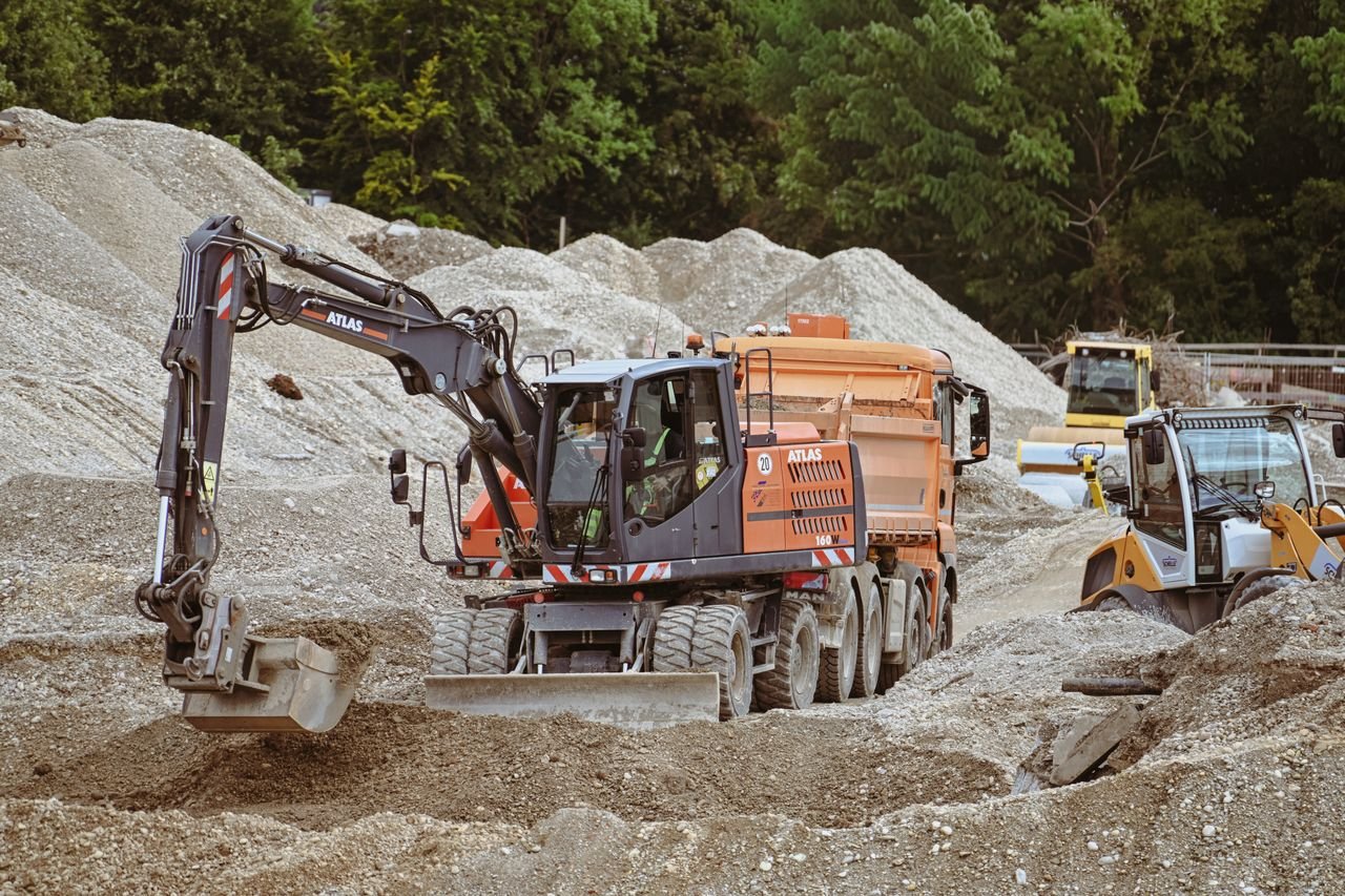 Excavator and machinery at a bustling construction site with piles of sand.